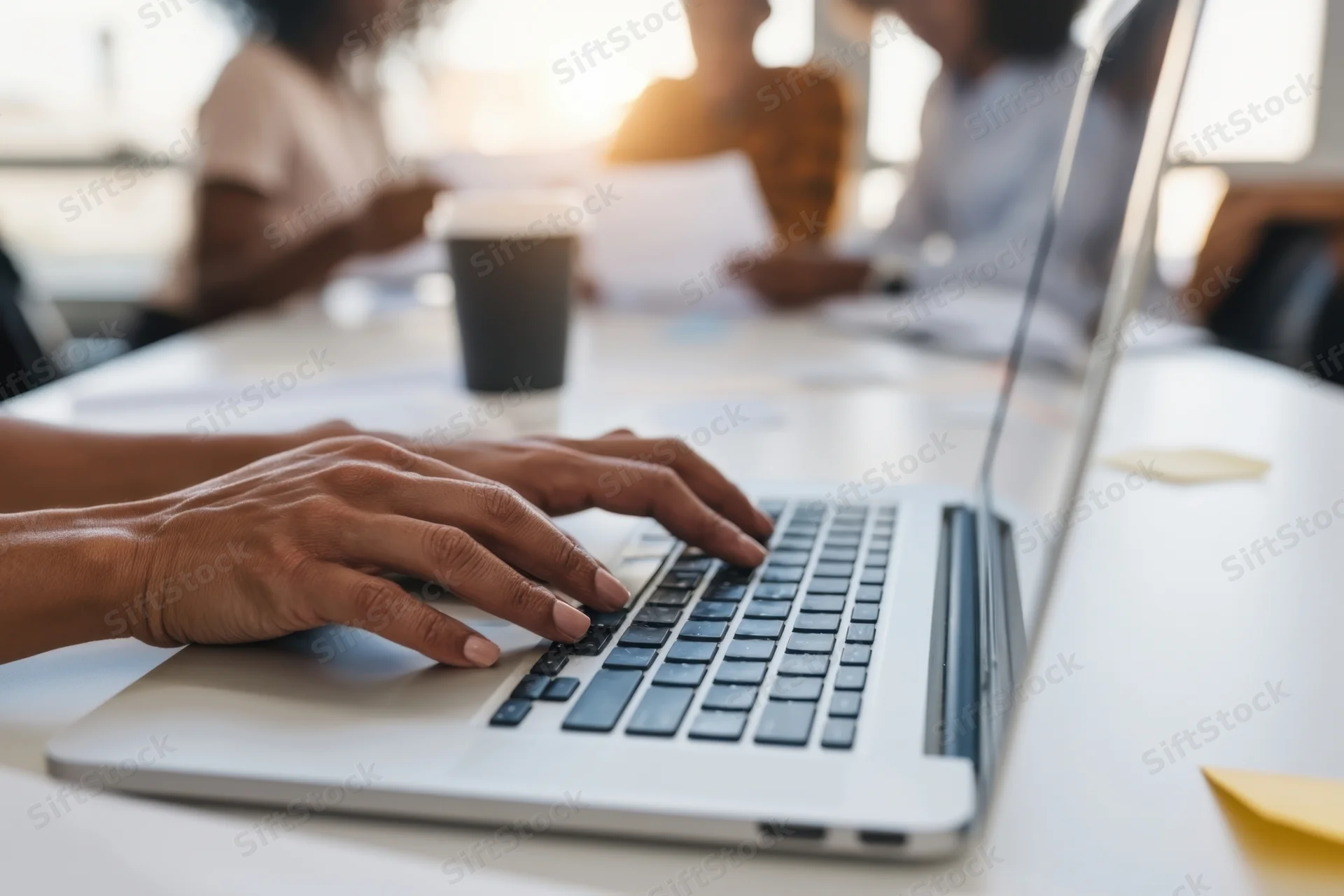 Hands typing on a laptop at a white desk in a bright office meeting room