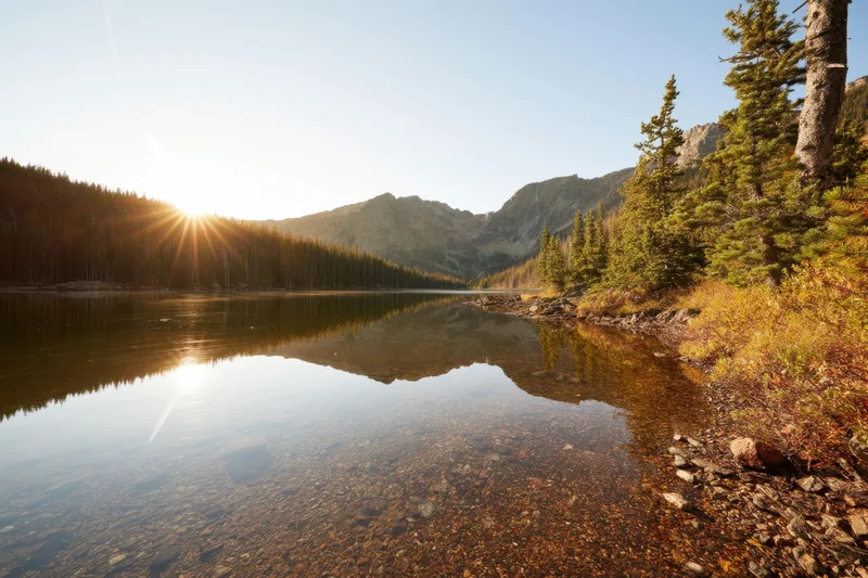 Alpine lake reflecting pine trees and rugged mountains at sunrise