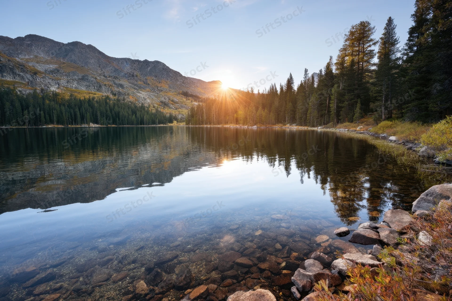 Crystal-clear alpine lake reflecting pine trees and rugged mountains at sunrise