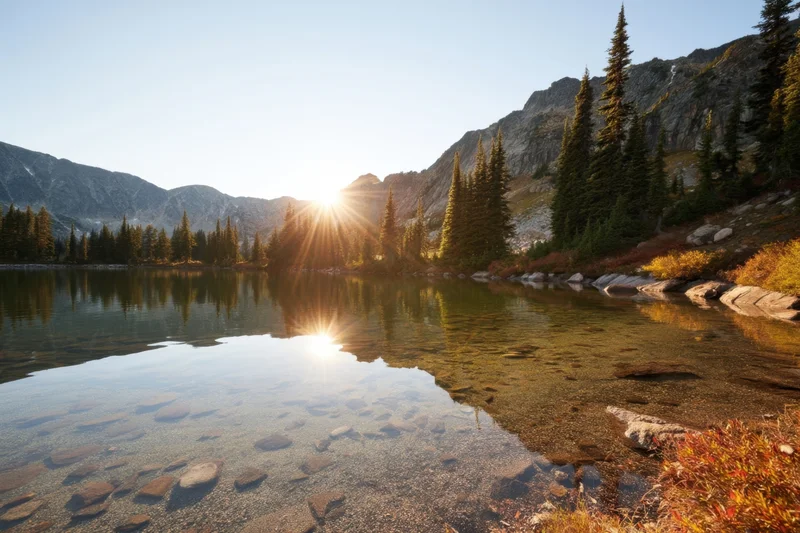 Crystal clear alpine lake reflecting pine trees and rugged mountains at sunrise