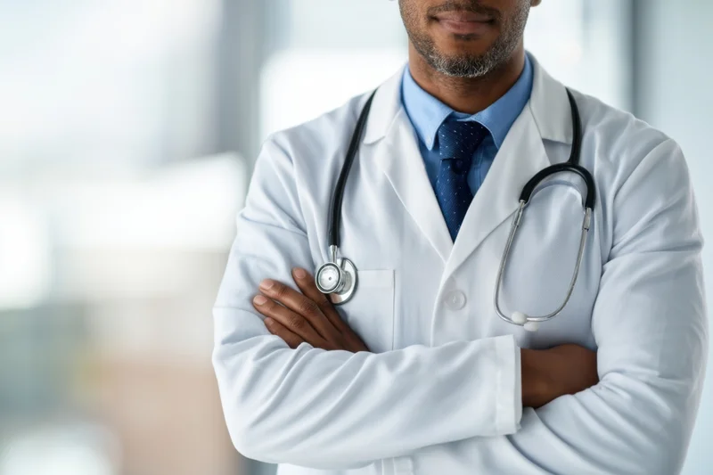 Doctor in white coat with arms crossed and stethoscope around neck in clinic setting
