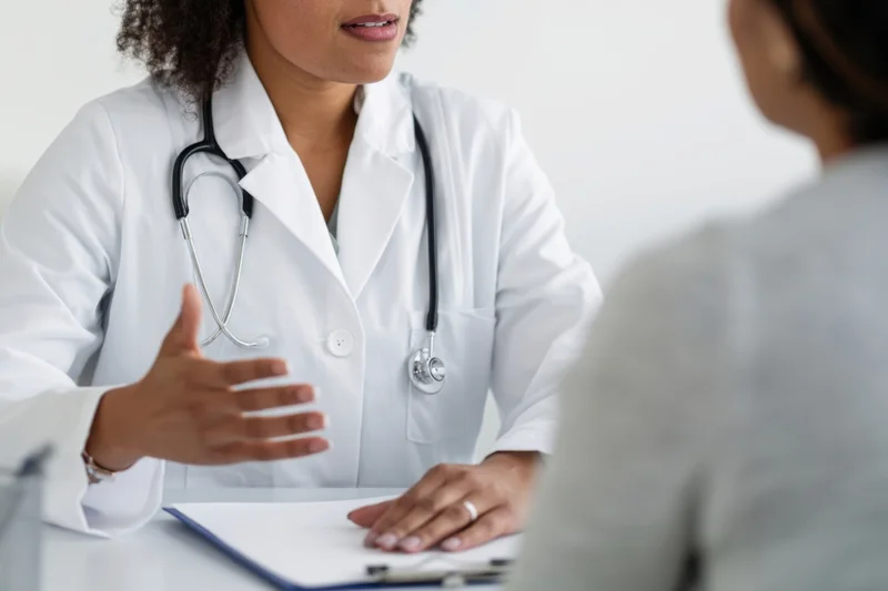 Female doctor in white coat discussing with patient at clinic desk