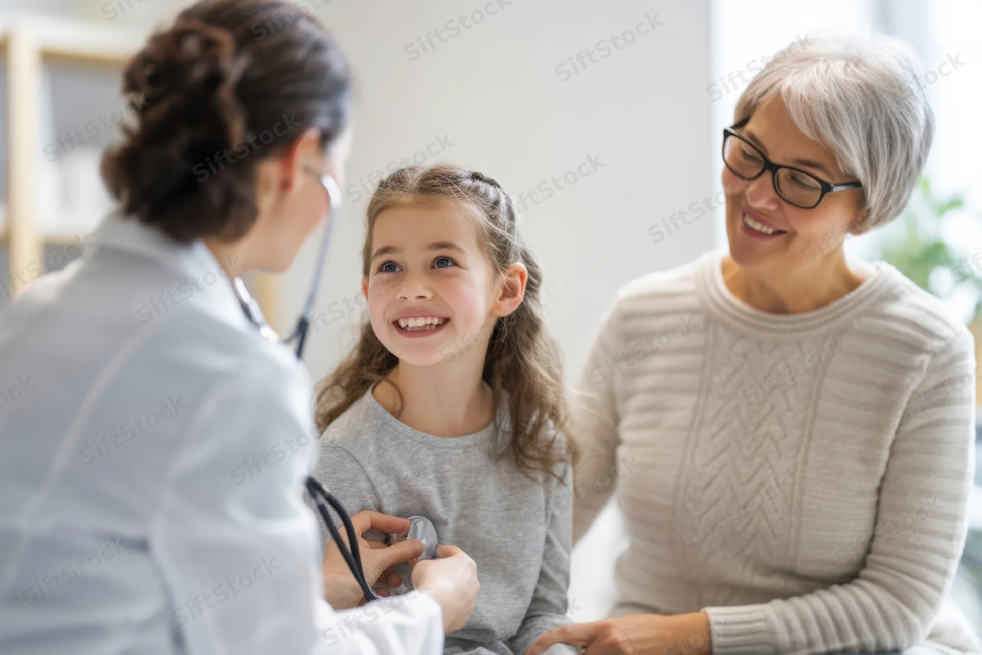 Pediatrician examining a smiling girl with stethoscope while mother looks on in clinic