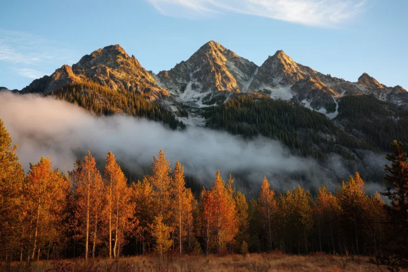 Jagged granite mountain peaks rising above a fog-filled valley with autumn aspen trees in the foreground