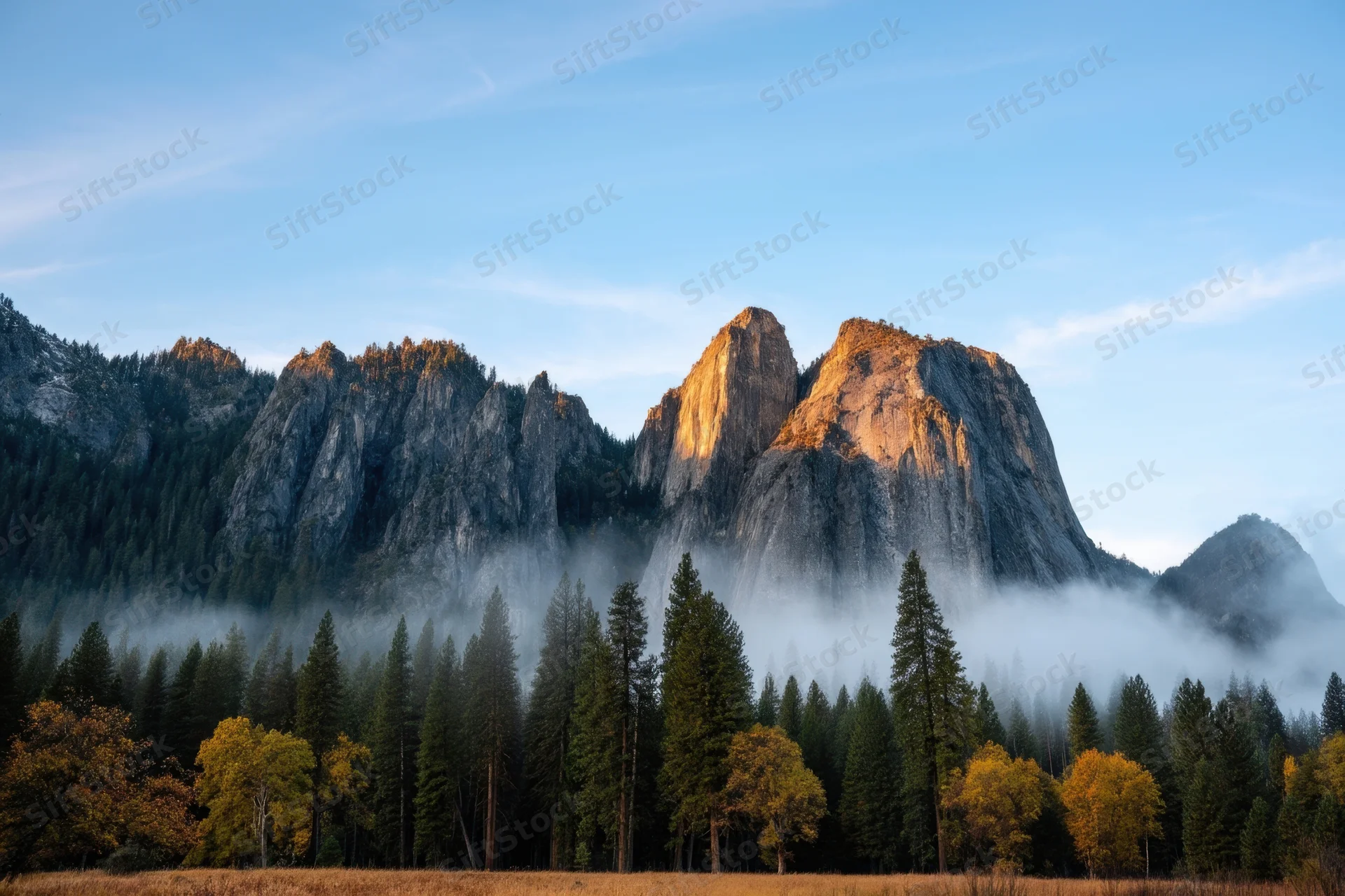 Jagged granite peaks rising above a misty valley with autumn trees and blue sky