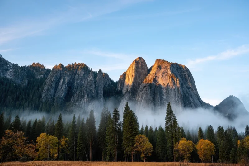Jagged granite peaks rising above a misty valley with autumn trees and blue sky