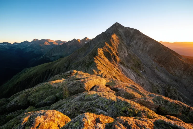 Rugged alpine peaks bathed in golden sunset light with distant valleys below