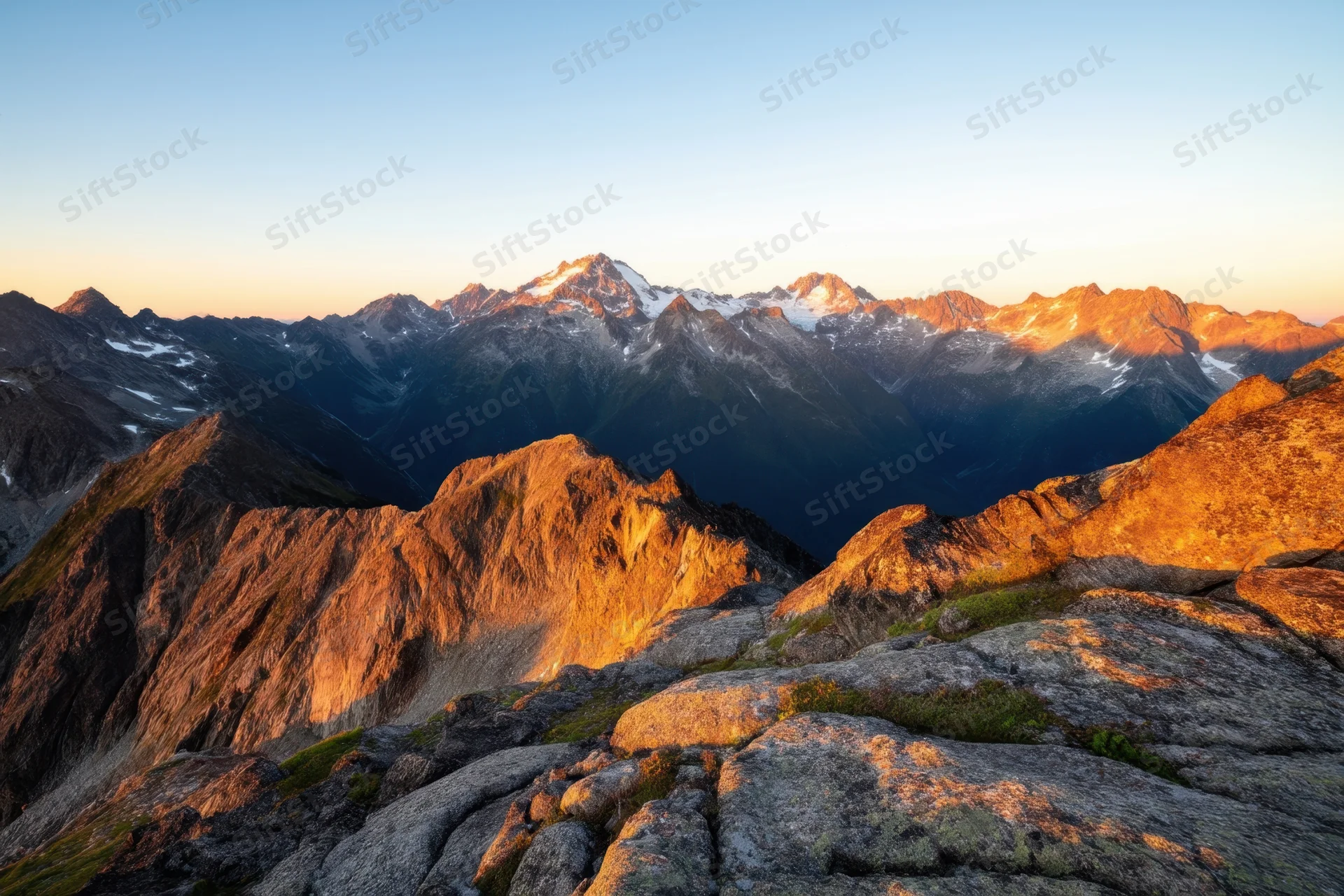 Rugged alpine peaks bathed in golden sunset light across a vast mountain range