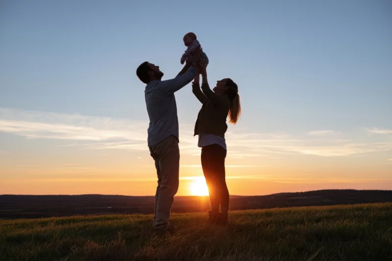 Parents lifting baby into the air at sunset on a grassy hill