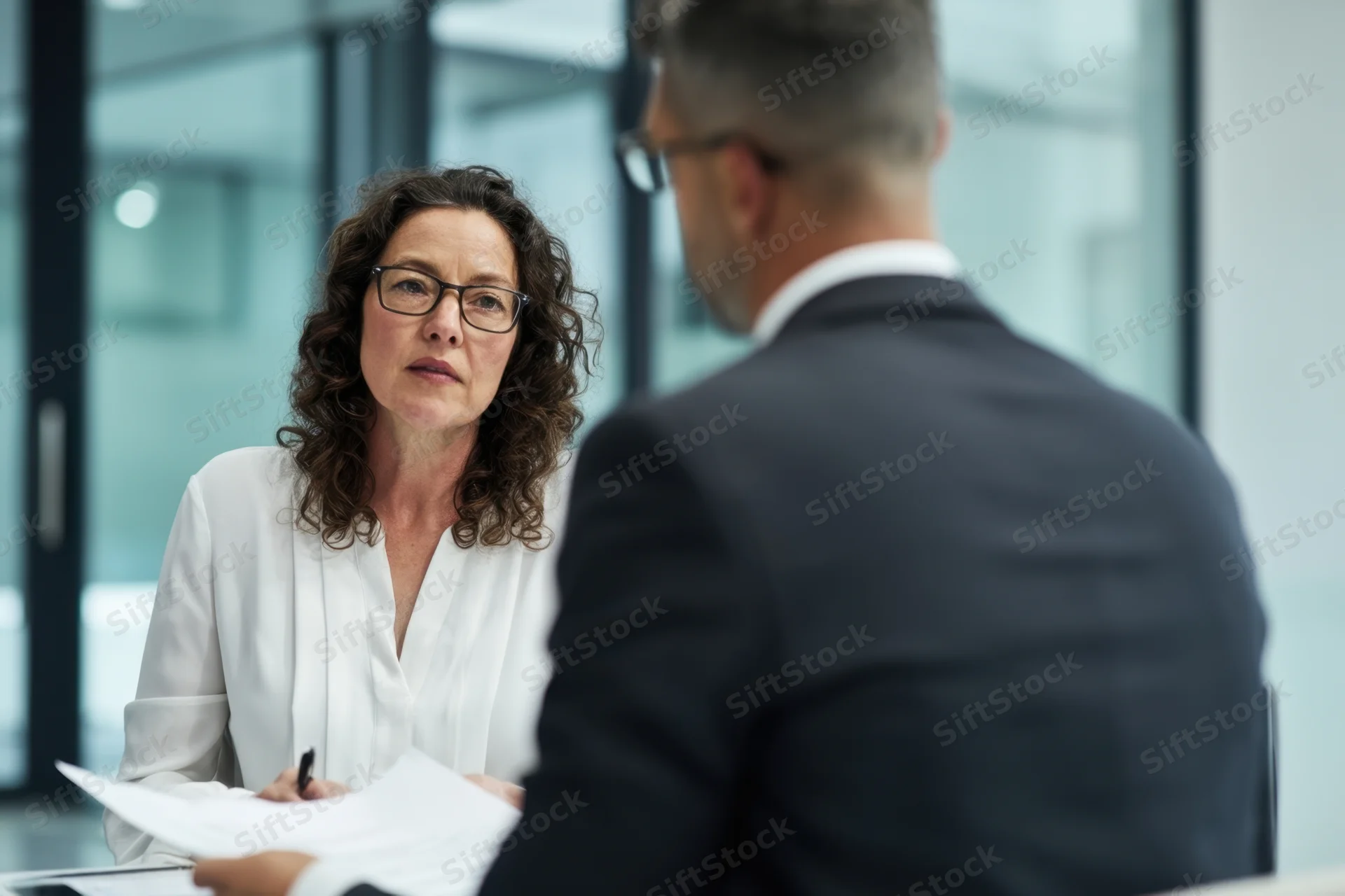 Woman in white blouse discussing documents with man in suit at office desk