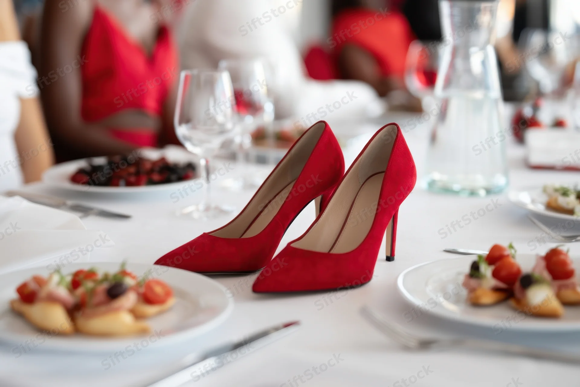 Red suede high heels on a formal banquet table with appetizers and wine glasses