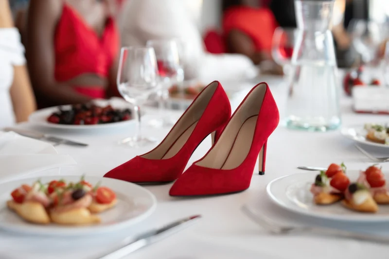 Red suede high heels on a formal banquet table with appetizers and wine glasses