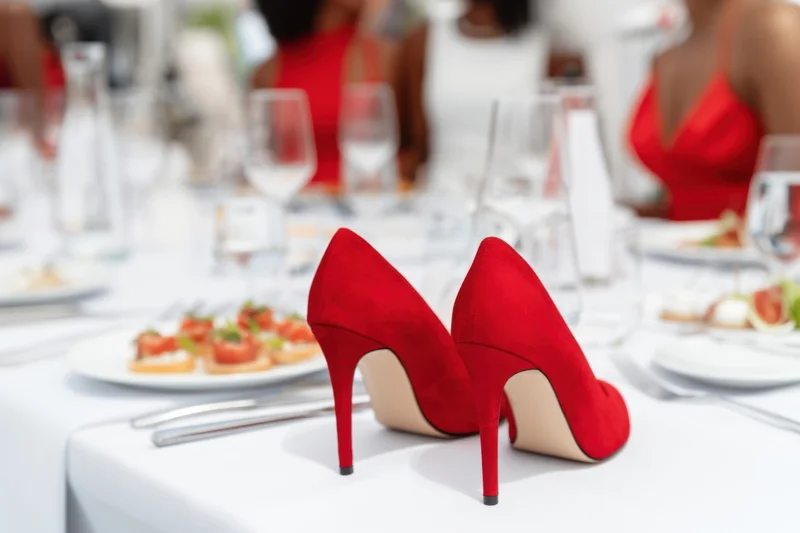 Red high-heeled shoes on a formal banquet table with guests in the background
