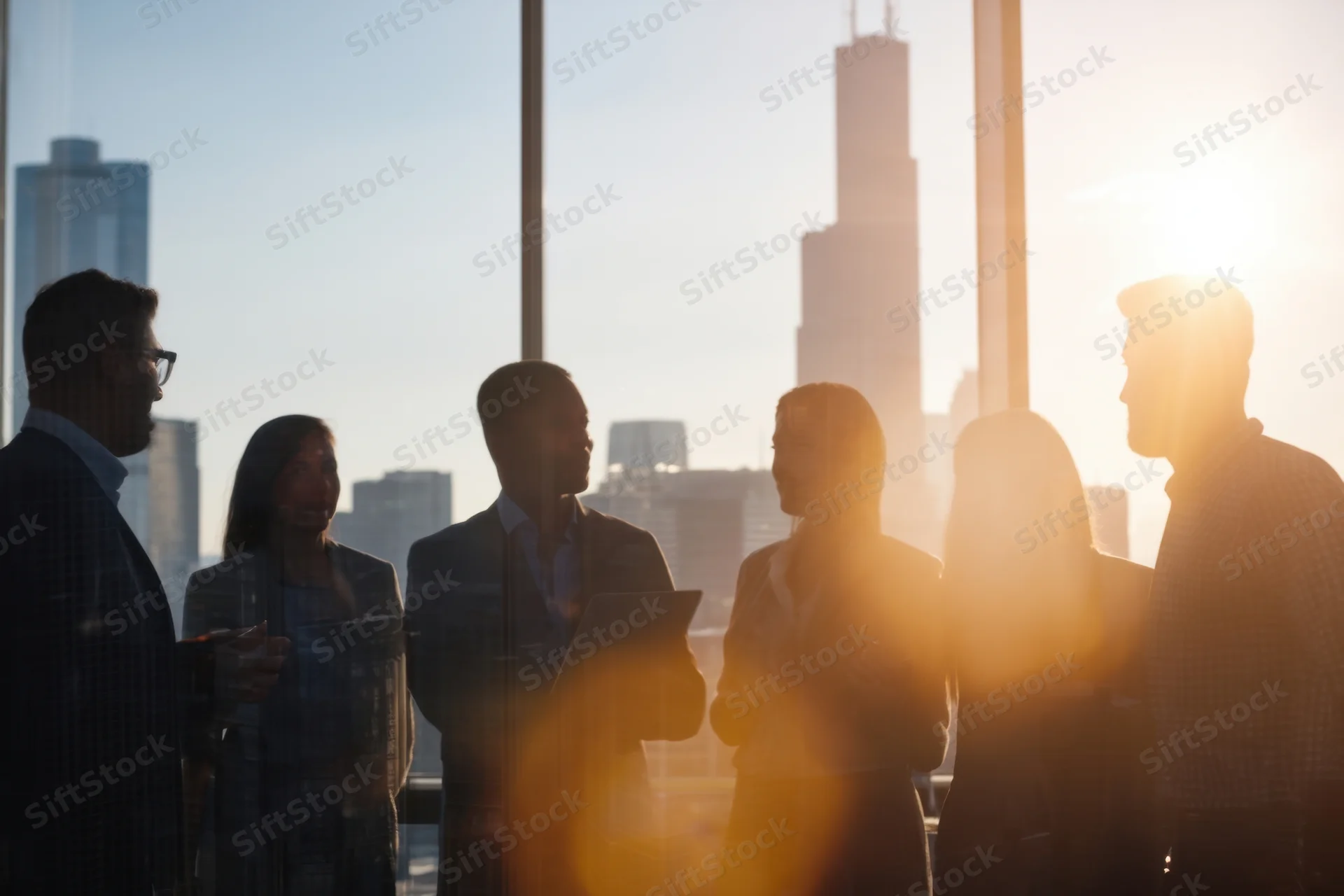 Silhouetted professionals in a meeting by a city skyline window at sunset