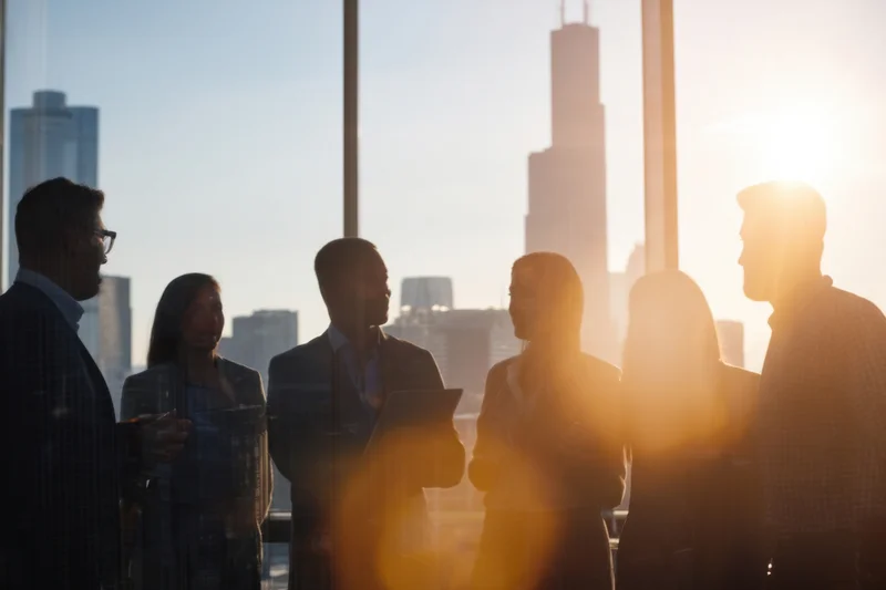 Silhouetted professionals in a meeting by a city skyline window at sunset
