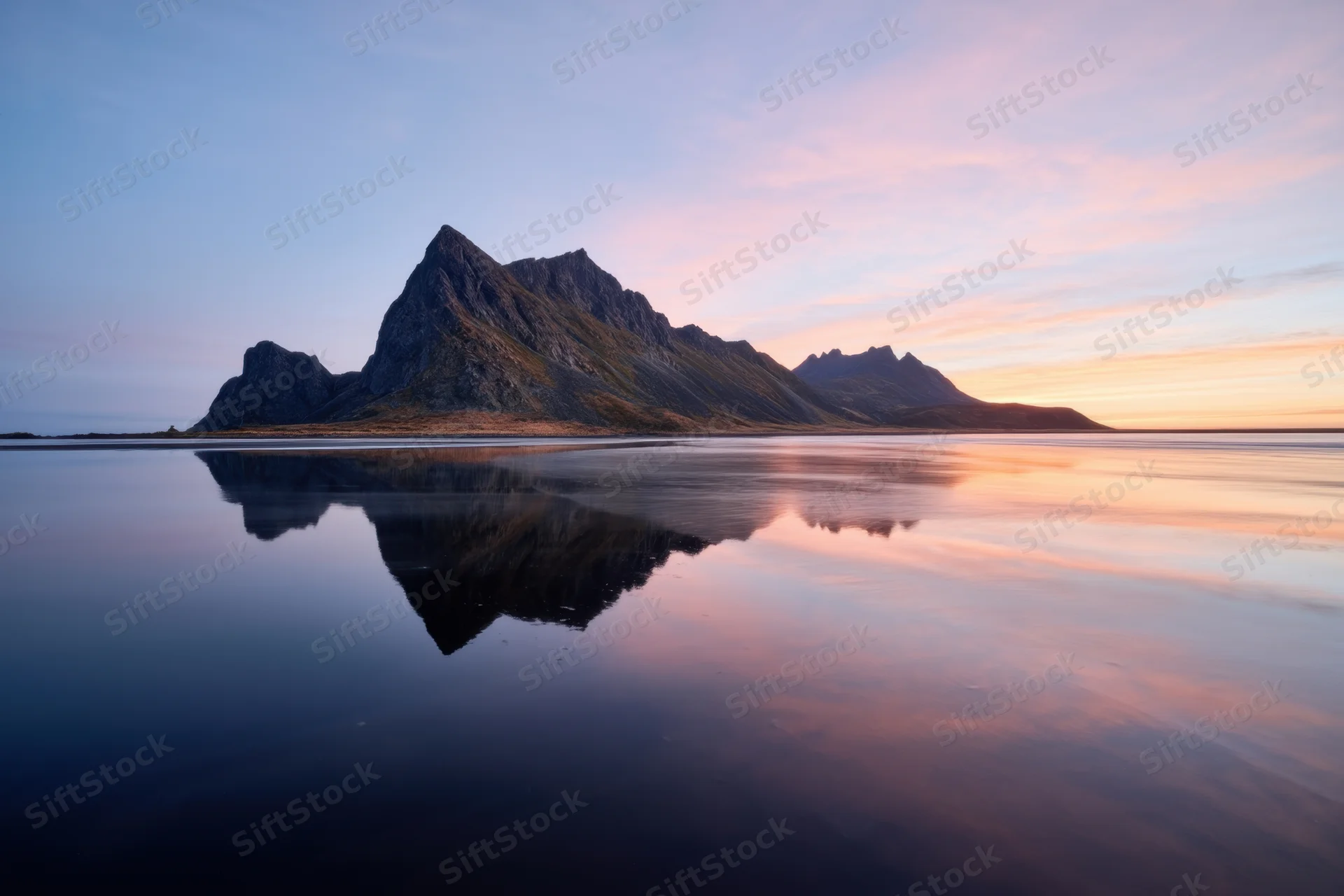 Jagged mountain island reflected in still sea at twilight