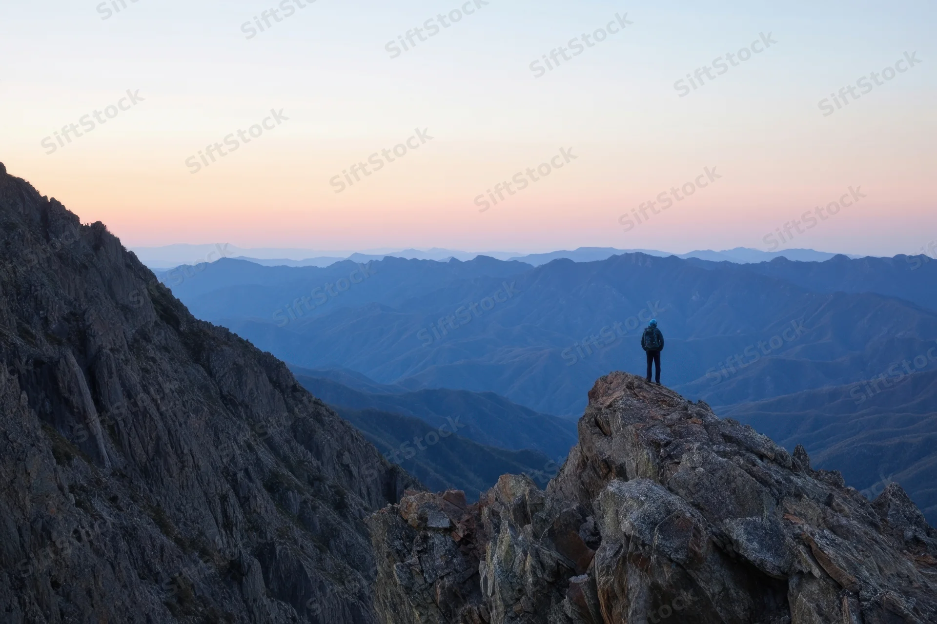 Hiker standing on rocky peak overlooking mountain range at sunset