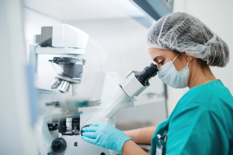 Woman researcher examining sample under microscope in laboratory