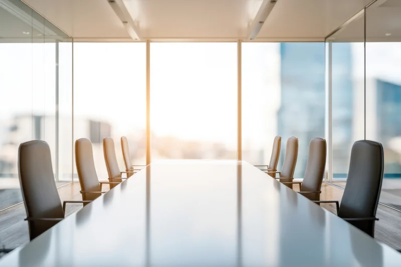 Long white conference table with chairs arranged along sides in modern office boardroom with glass walls and city view