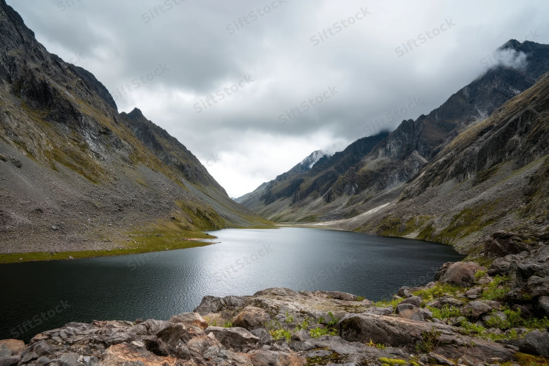 Alpine valley with calm dark lake flanked by rugged mountains under overcast sky
