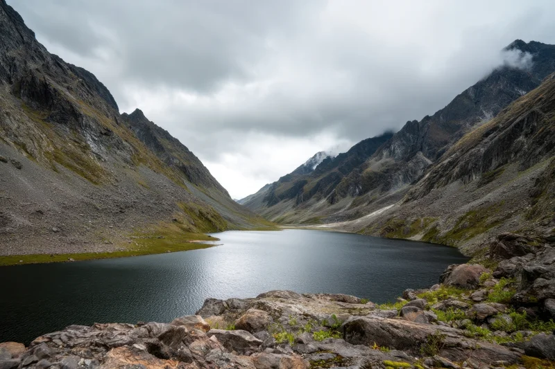 Alpine valley with calm dark lake flanked by rugged mountains under overcast sky