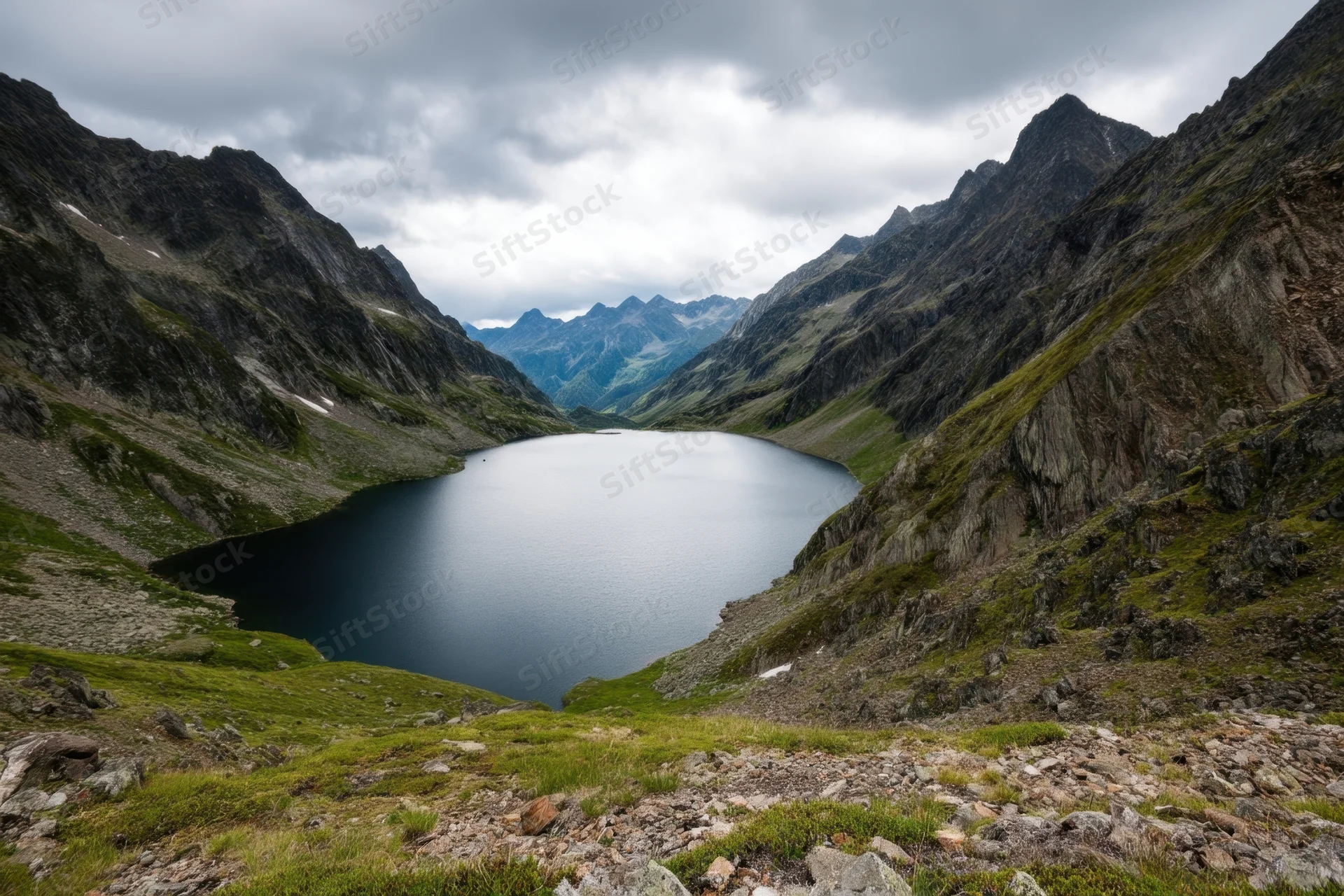 Alpine valley with calm dark lake flanked by rugged mountains under overcast sky