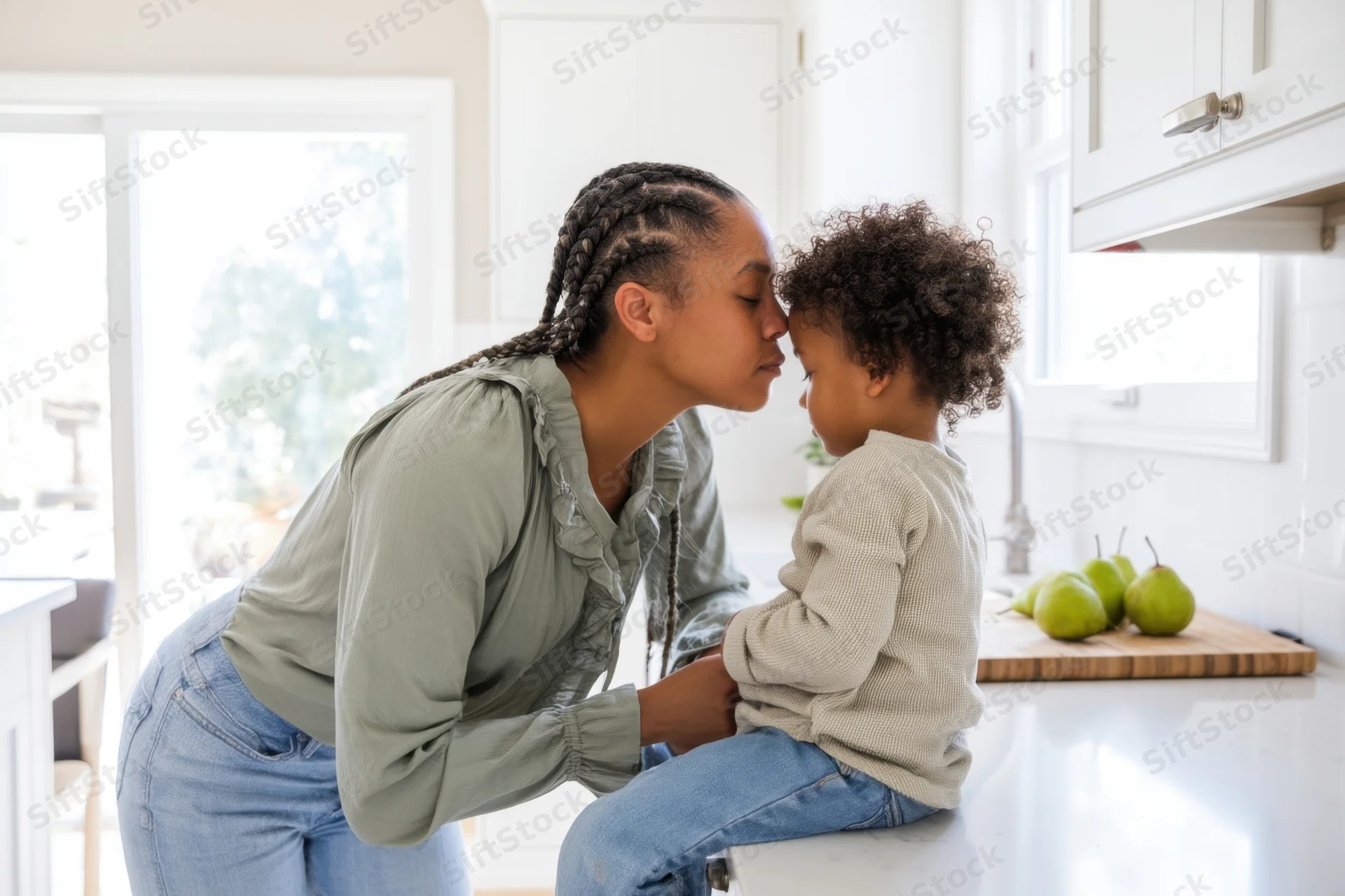 Mother kissing toddler on the forehead in kitchen
