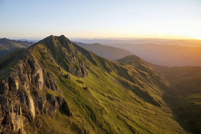 Panoramic view of rugged mountain peaks and green valleys at sunset