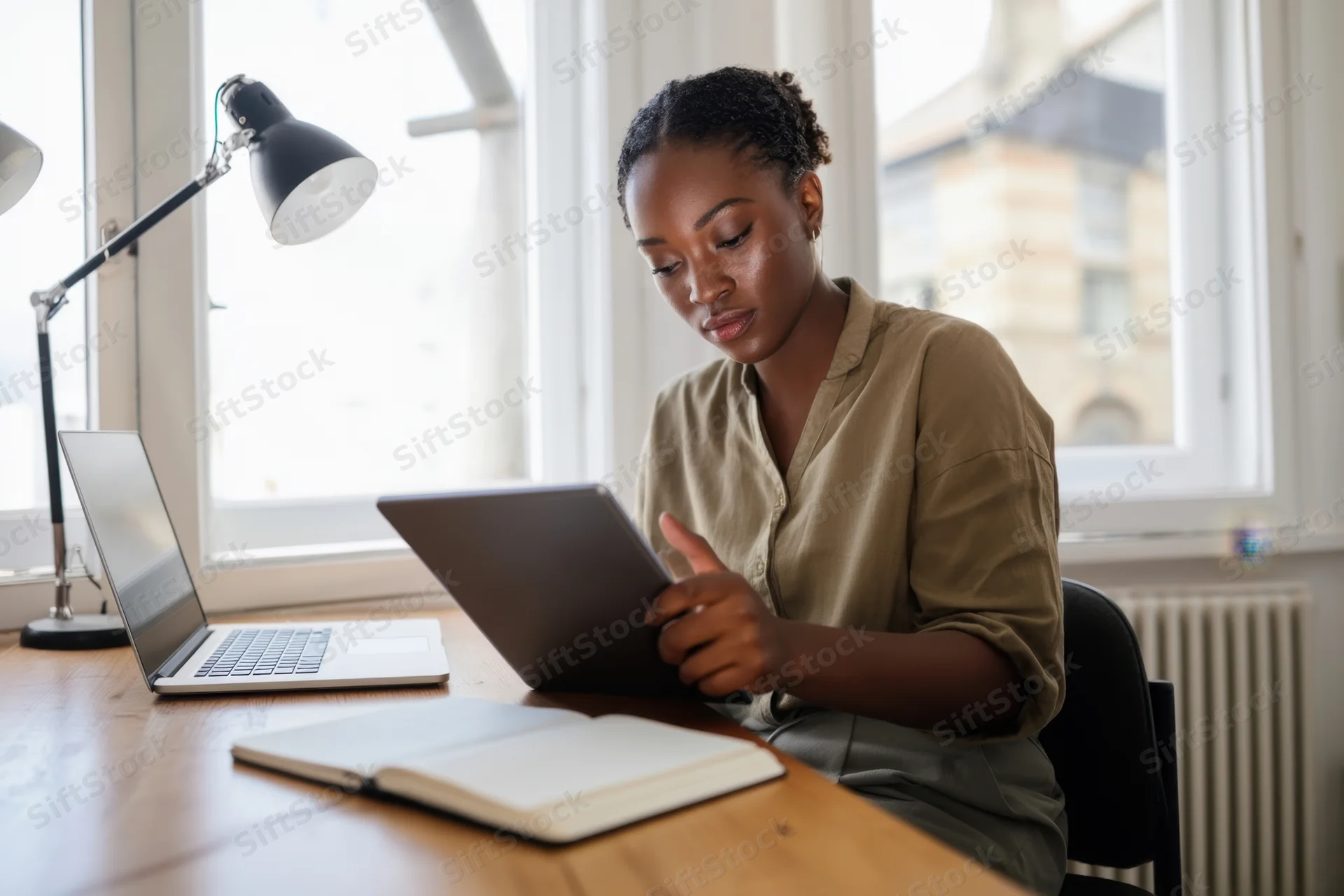 Woman tapping tablet at wooden desk with laptop and notebook nearby