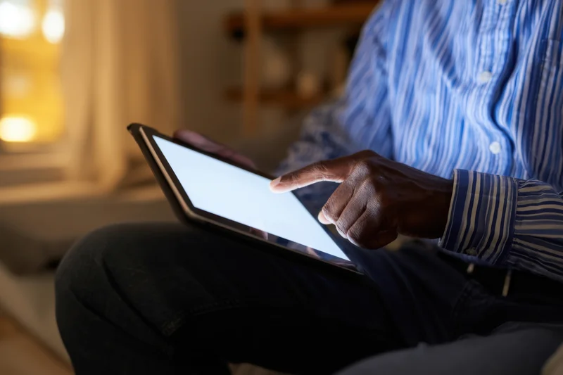 Man using tablet on his lap in a dimly lit room at home