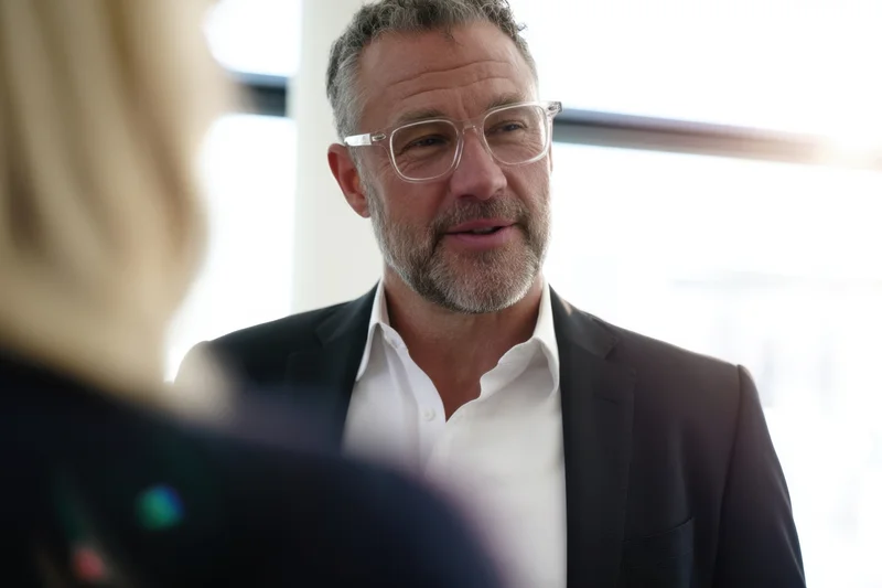 Man in suit and glasses conversing with a colleague in an office setting