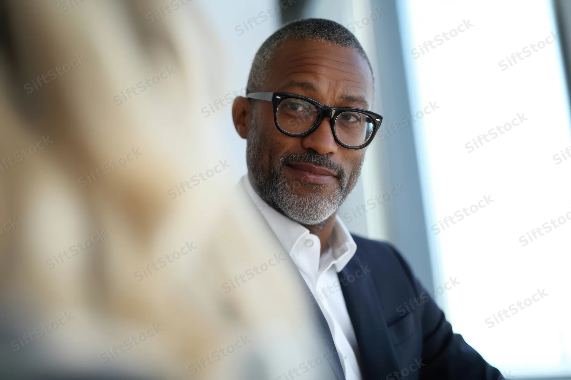 Man in suit and glasses looking at another person in an office setting