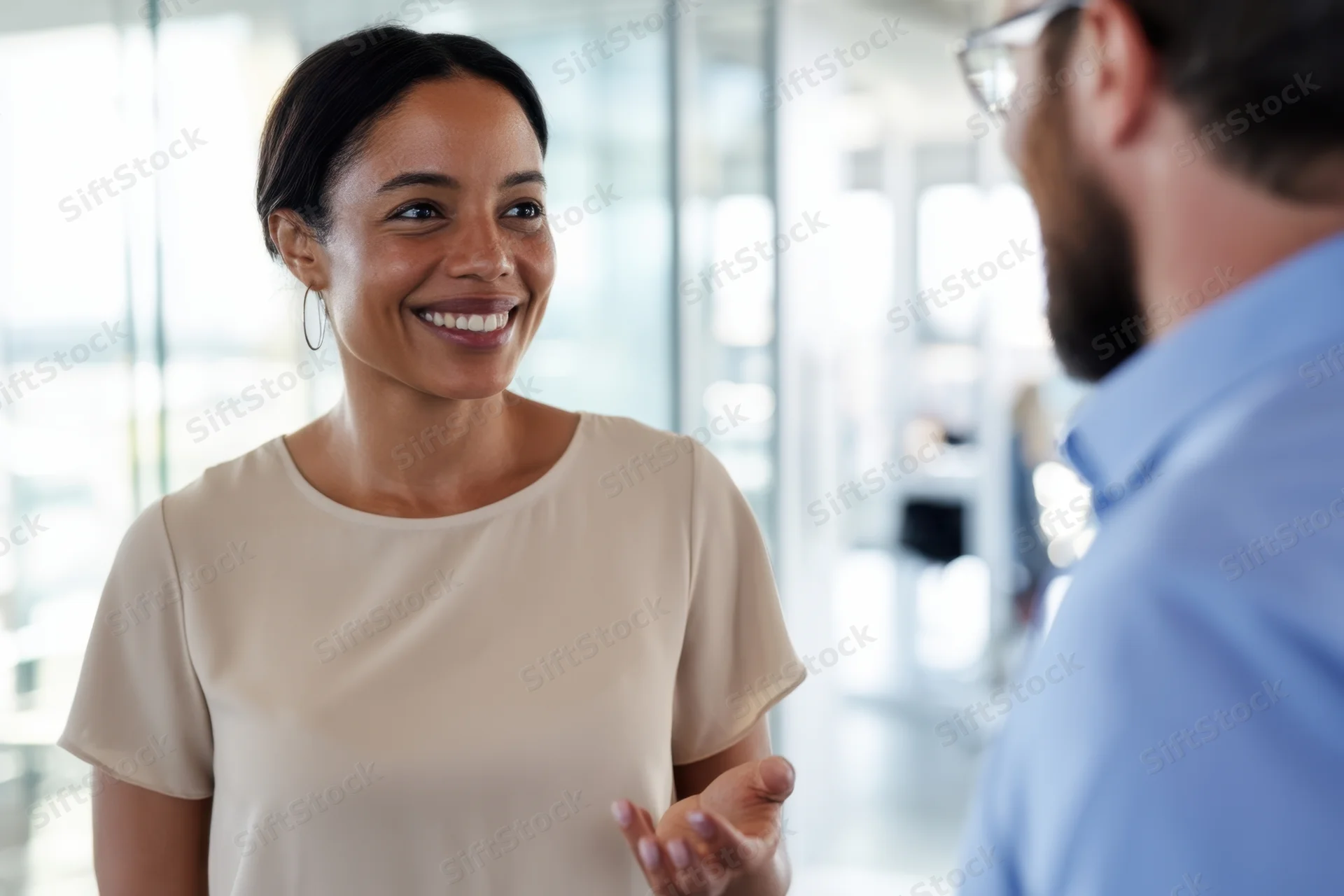 Woman smiling and gesturing during conversation with colleague in office