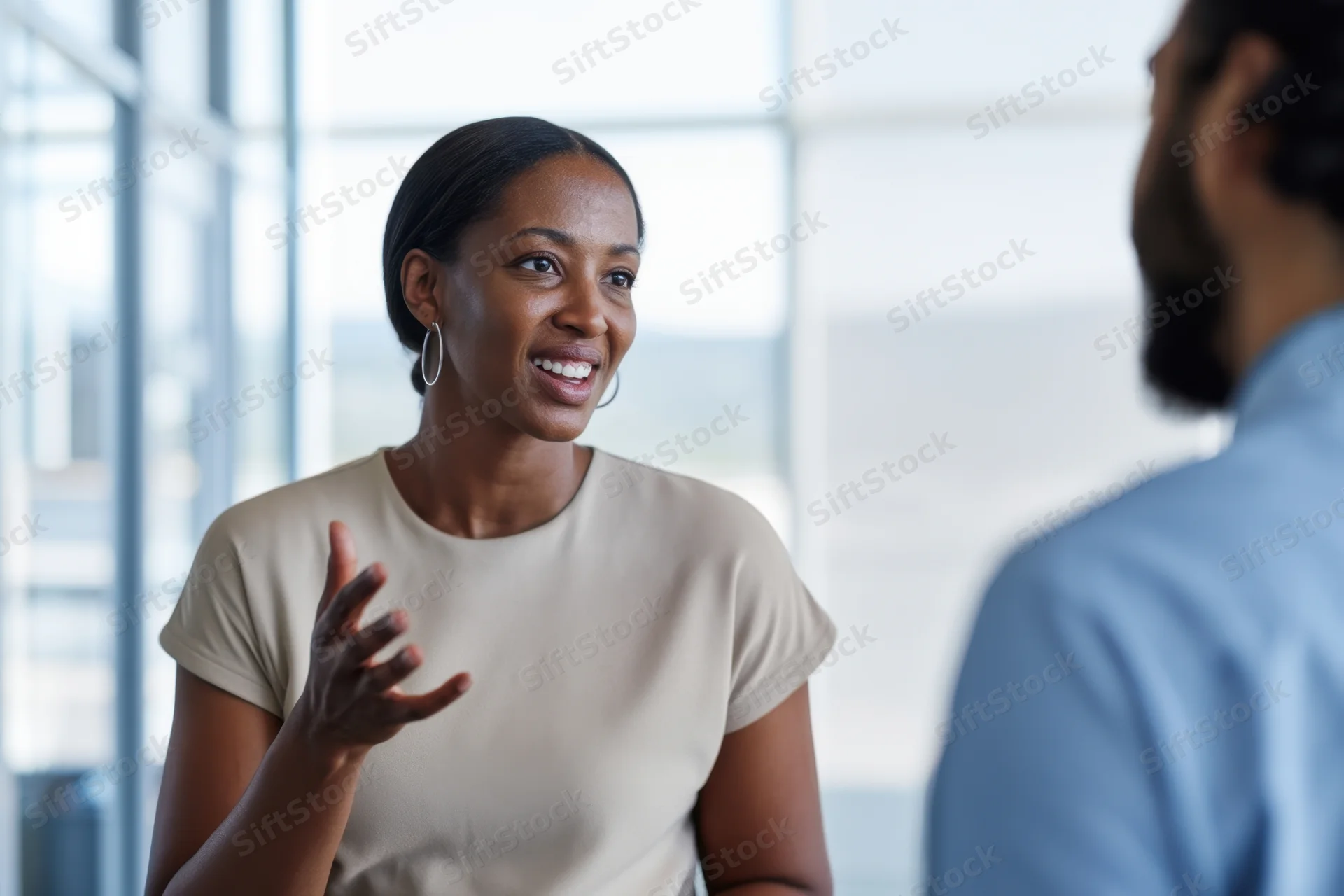 Woman smiling and gesturing during conversation with colleague in office setting