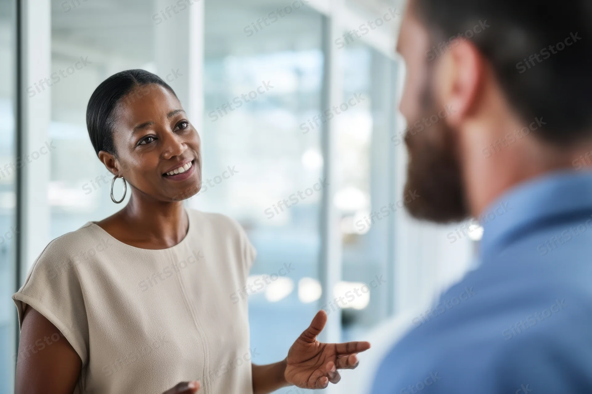 Woman smiling and gesturing during conversation with colleague in modern office