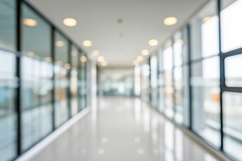 Modern office hallway with glass walls and recessed ceiling lights, glossy white floor reflecting light