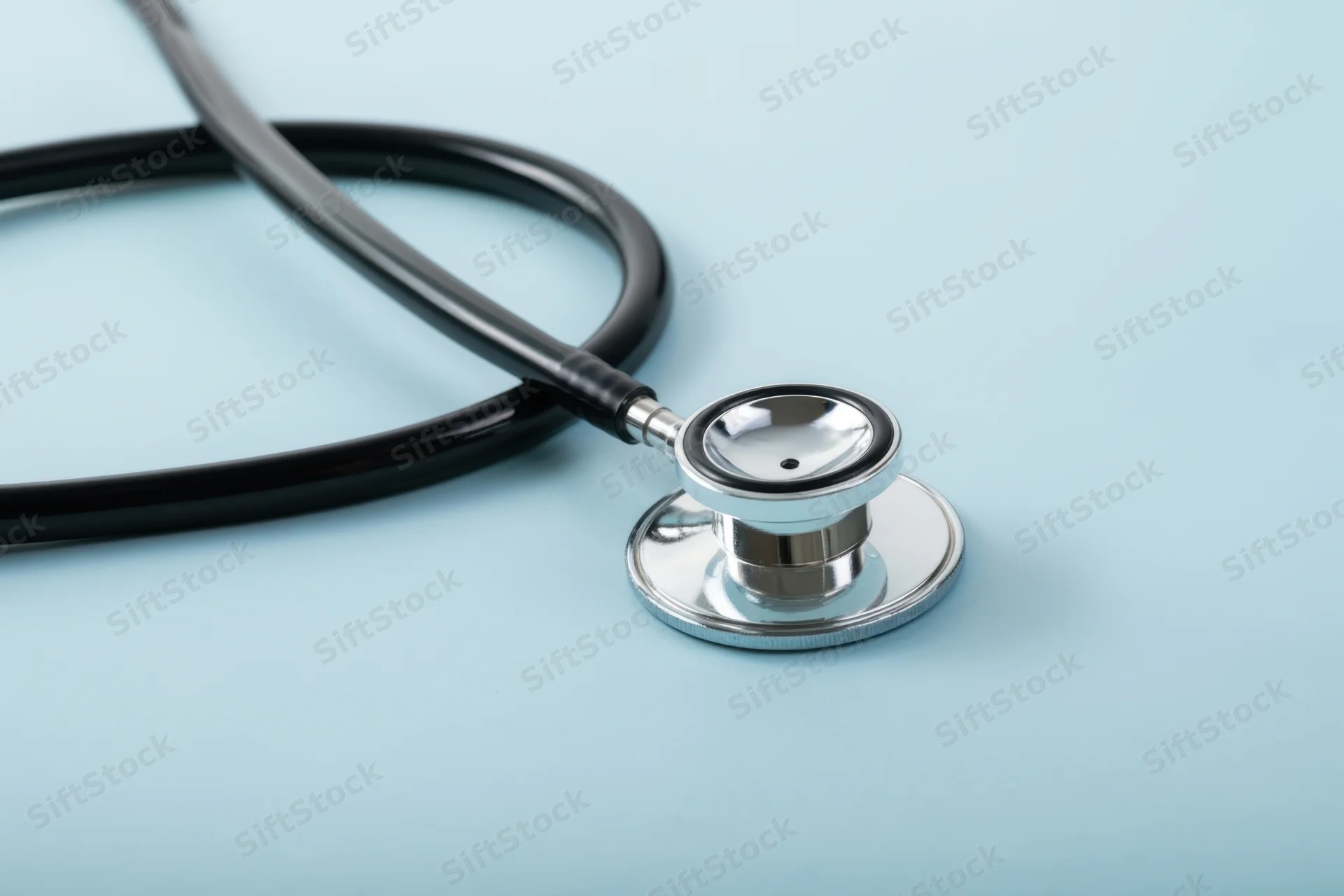 Stethoscope with black tubing and silver chest piece resting on a light blue surface