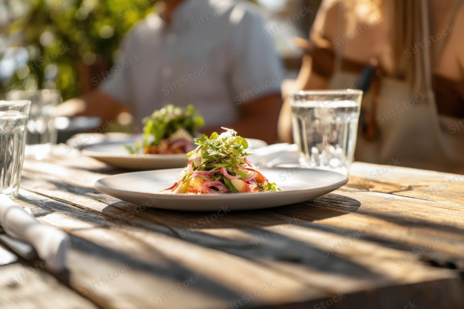 Salad served on a rustic wooden table outdoors with couple dining in background