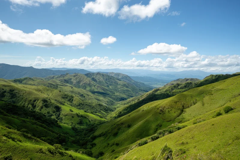 Rolling green hills forming a valley under a bright blue sky with scattered clouds