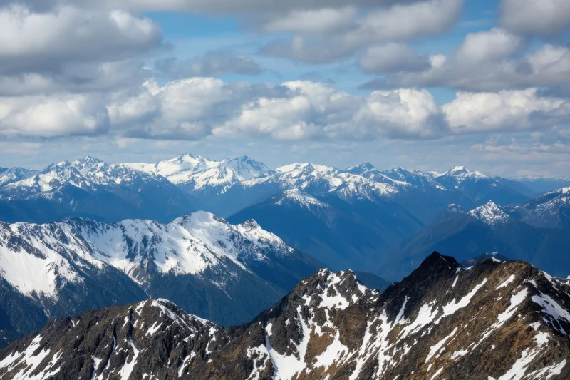 Snow-capped alpine peaks rising in layered ridges under a partly cloudy sky