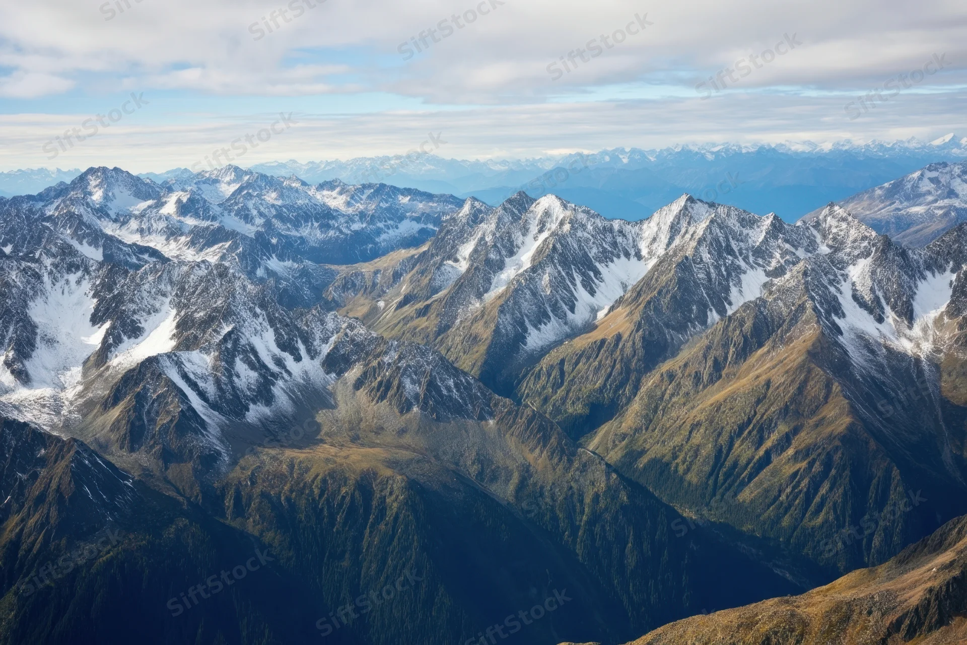 Sweeping alpine panorama with snow-capped peaks and forested valleys under a partly cloudy sky