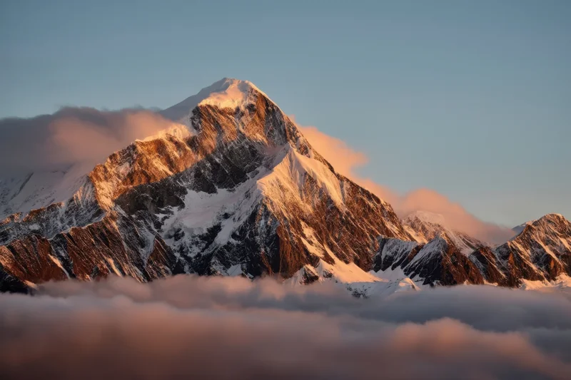 Snow-capped mountain peak rising above a sea of clouds at sunrise