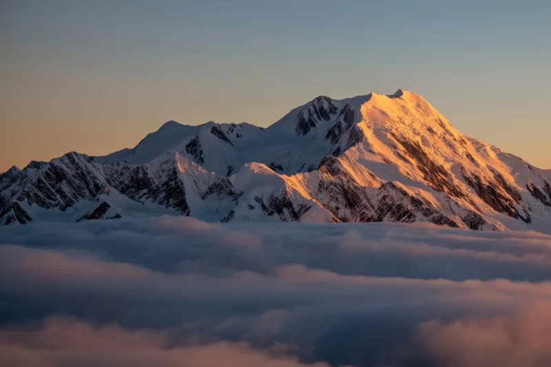 Snow-capped mountain peak rising above a sea of clouds at sunrise