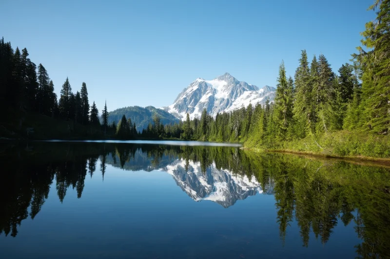 Tranquil alpine lake mirrors a snow capped mountain range forest