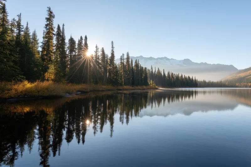 Alpine lake reflecting pine forest and snow-capped mountains at sunrise
