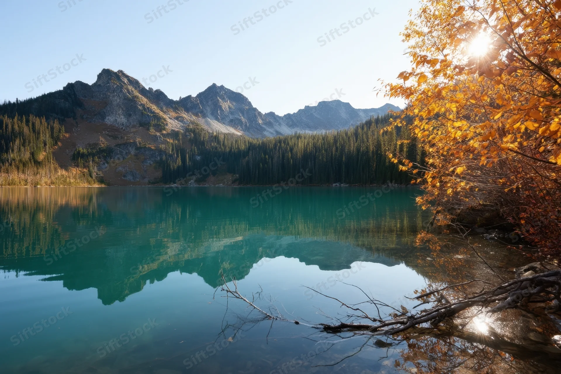 Tranquil alpine lake reflecting mountains and autumn trees under clear sky