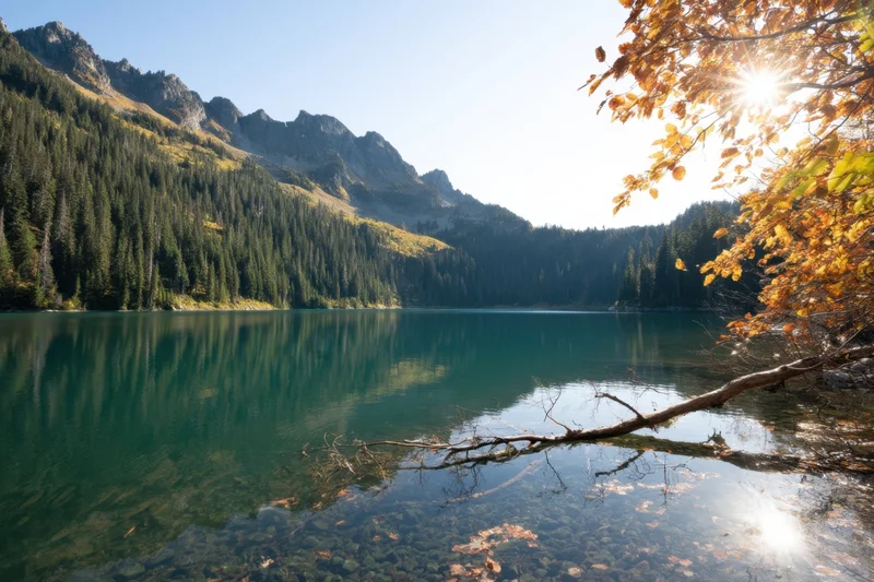 Tranquil alpine lake with turquoise water reflecting mountains and autumn trees under sunlight