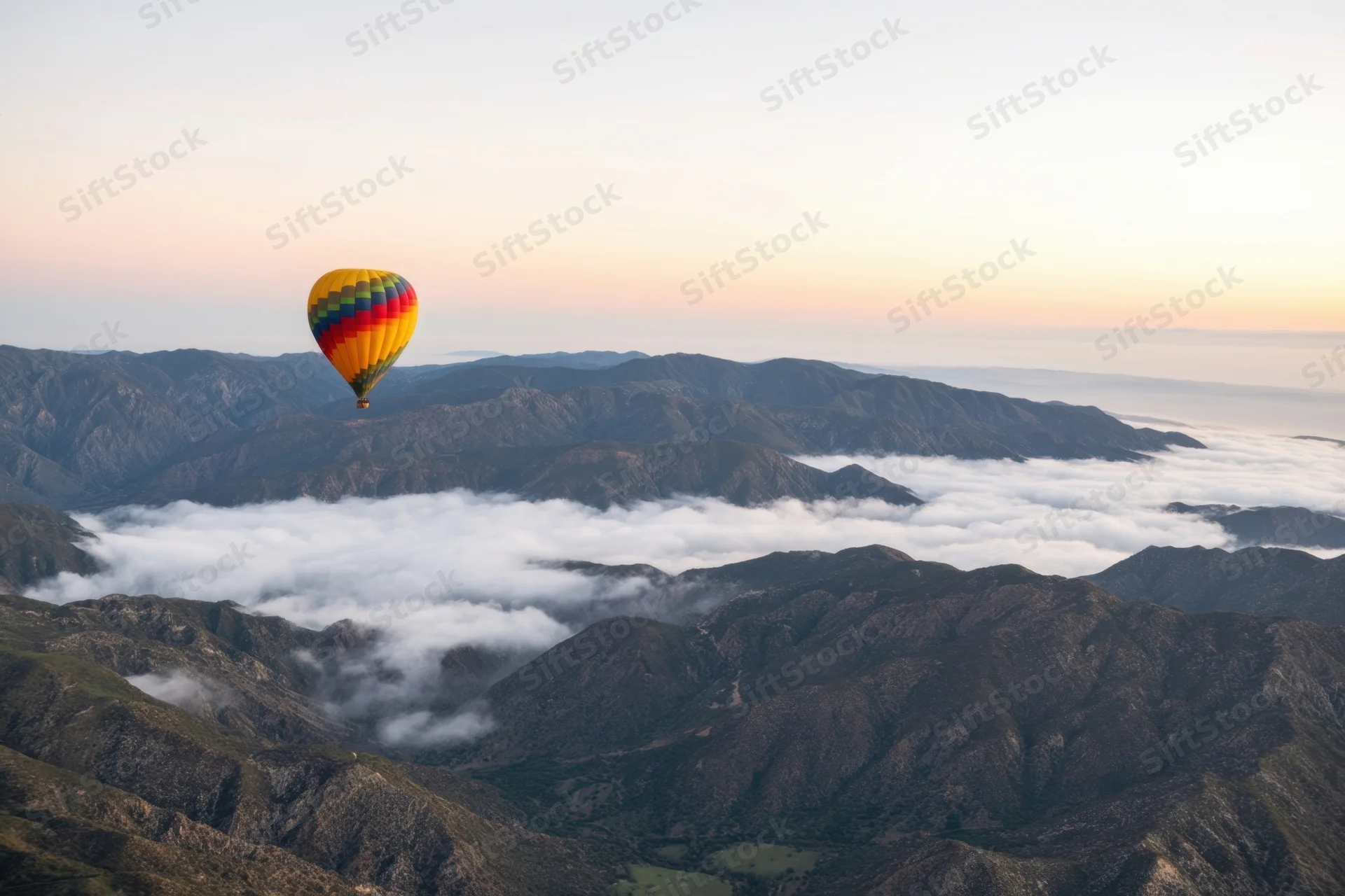 Hot air balloon floating over mountain range above clouds at sunrise
