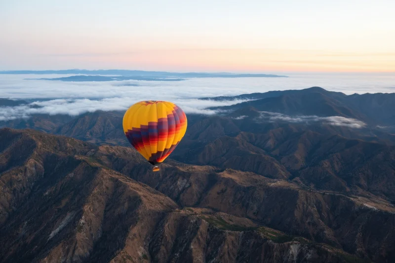 Hot air balloon floating above mountain range with clouds below at sunrise