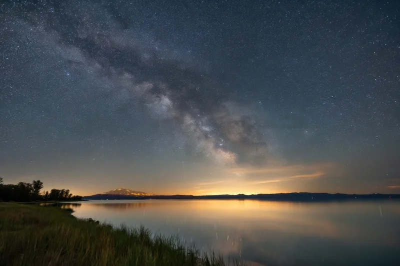 Star-filled night sky over a calm lake reflecting distant mountain under milky way